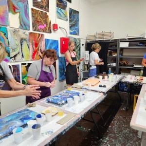People in a studio working on art pieces with resin and paint on tables.