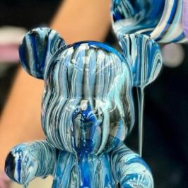 Hands pouring blue and white paint on a small bear-shaped figure.