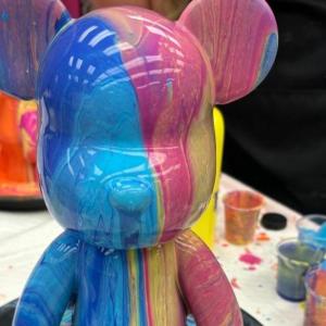 Multicolored bear sculpture with paint dripping, surrounded by paint cups.