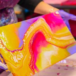Person holding vibrant abstract painting with pink, yellow, and orange swirls.
