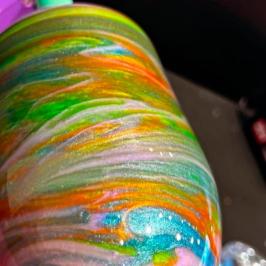 Colorfully swirled tumbler with glittery patterns on a pink surface.