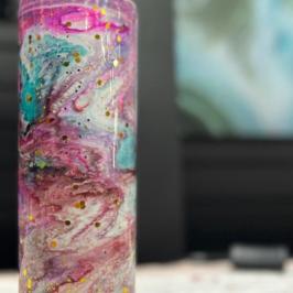 Colorful, abstractly painted tall tumbler with swirls on a table.
