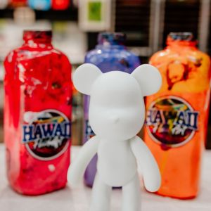 White bear figurine in front of colorful paint bottles on a table.