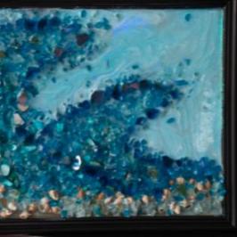 Framed mosaic artwork of an ocean wave, with books on shelves in the background.