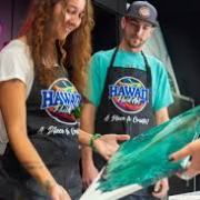 Two people in aprons, one holding a canvas with green paint, smiling and engaged in an art activity.